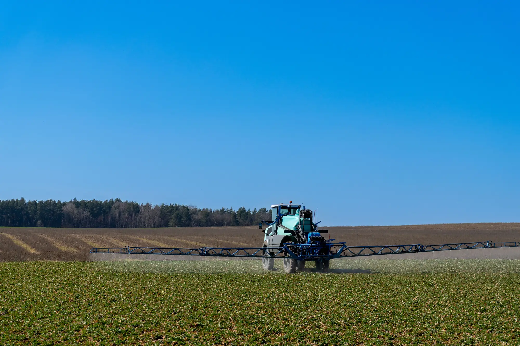 A self-propelled sprayer with its boom folded out, working across spring ground